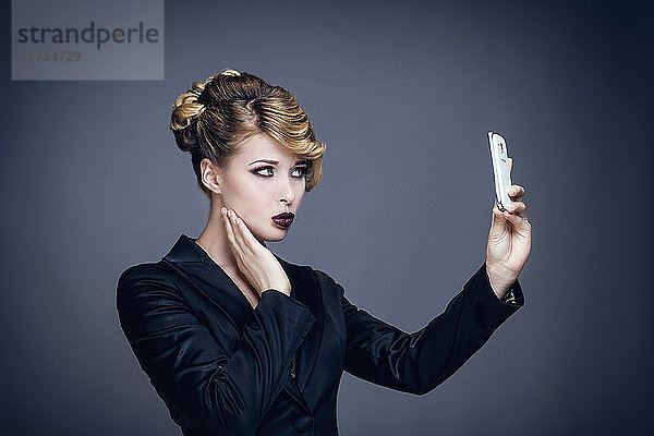 Porträt einer jungen Frau im Profil,  die ein Foto mit ihrem Mobiltelefon macht