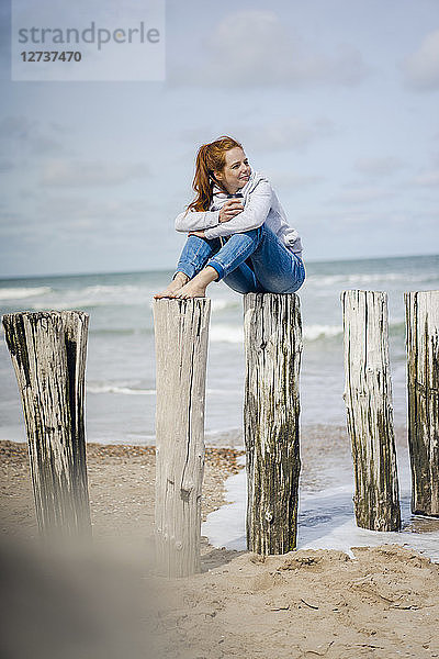 Woman sitting on fence at the sea,  drinking tea