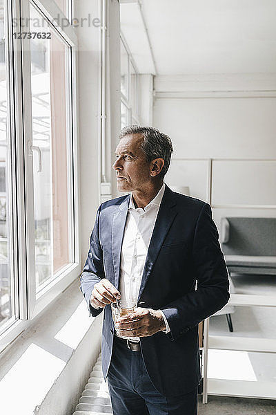 Mature businessman with glass of coffee in his office looking out of window