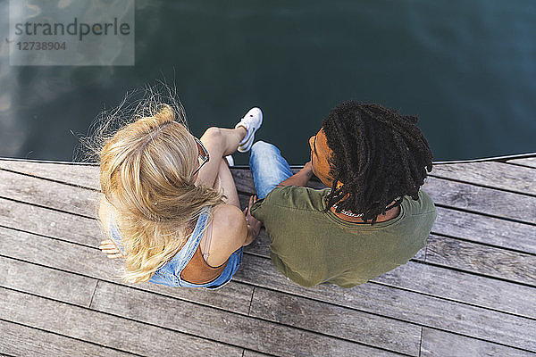 Multicultural young couple relaxing side by side on jetty,  top view