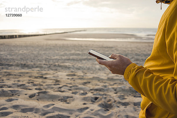 Man in yellow jacket,  using smartphone on the beach