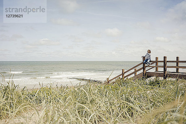 Woman sitting on fence at the beach,  relaxing at the sea