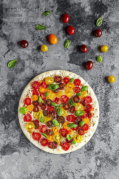Unbaked pizza with tomatoes and basil leaves