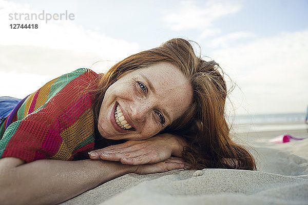 Redheaded woman lying in sand on the beach,  with eyes closed