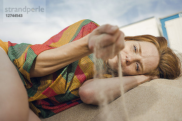 Redheaded woman lying on the beach,  with sand trickling through her hand