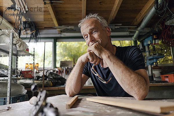 Portrait of confident mature man at workbench in his workshop