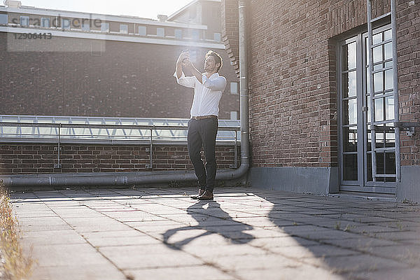 Businessman standing on rooftop terrace,  taking a selfie