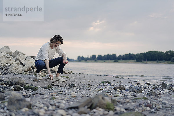 Woman crouching at the riverside,  drawing in sand with a stick