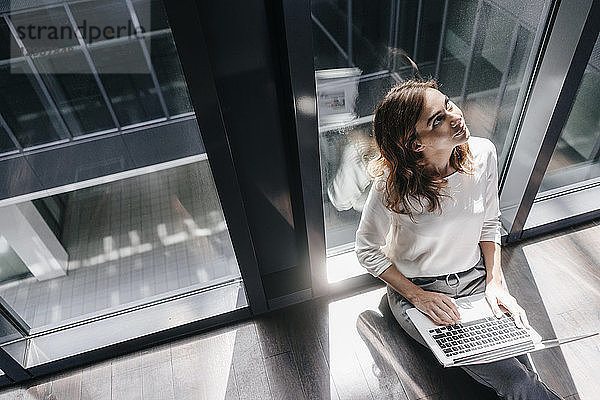 Businesswoman sitting on ground in empty office,  using laptop