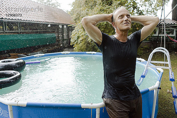 Mature man enjoying summer rain in garden at swimming pool