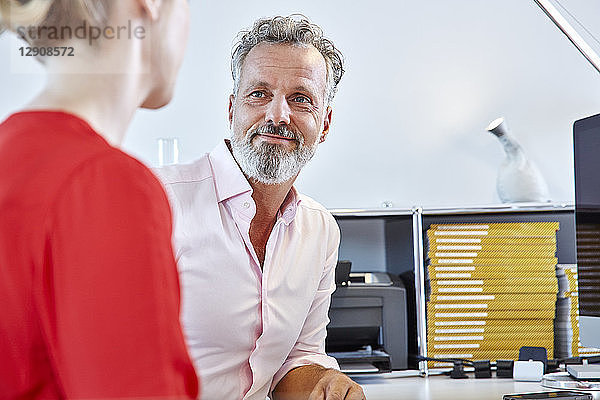 Mature man looking at female colleague at desk in office