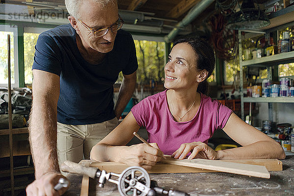 Smiling mature man watching woman working in workshop