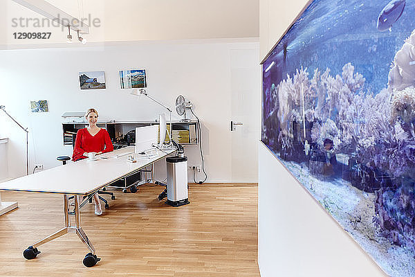Young woman sitting at desk in office with an aquarium