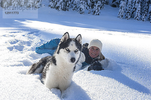 Austria,  Altenmarkt-Zauchensee,  portrait of smiling young woman lying with dog in snow