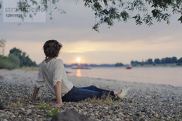 Woman sitting at the river,  watching sunset