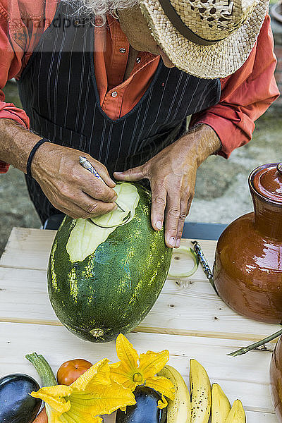 Senior man working on a watermelon with carving tool