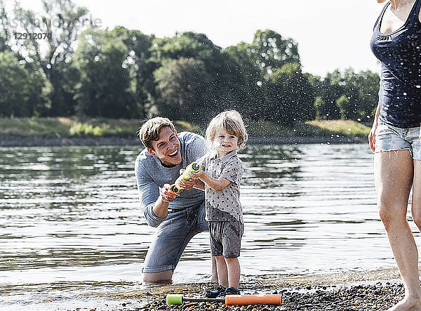 Father and son having fun at the riverside,  playing with a water gun