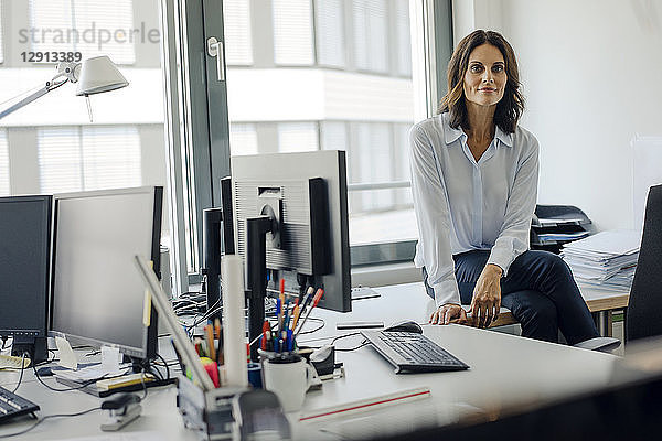 Mature businesswoman sitting o desk in office,  smiling