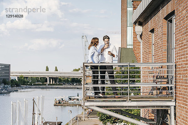 Business people standing on balcony,  using smartphone