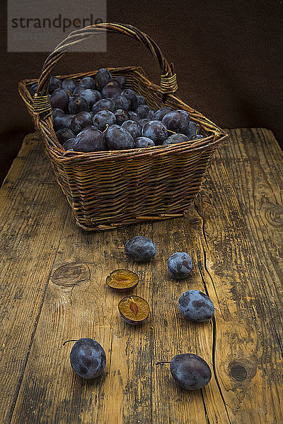 Wicker basket of organic plums,  wooden table