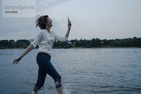 Laughing woman running at the riverside,  using smartphone