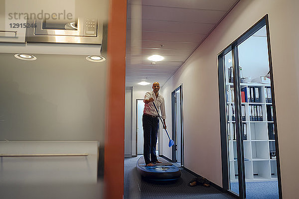 Businessman standing on paddle board,  exercising in office corridor