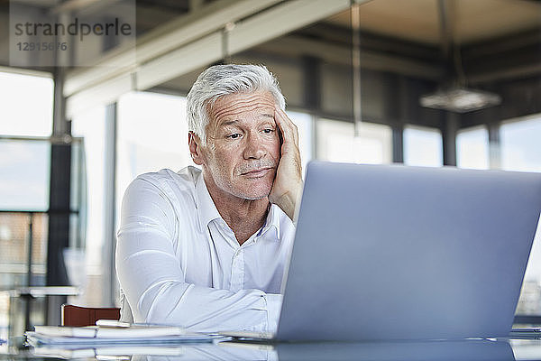 Bored businessman sitting at desk,  using laptop