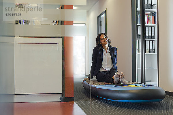 Businesswoman sitting on paddle board,  daydreaming in office