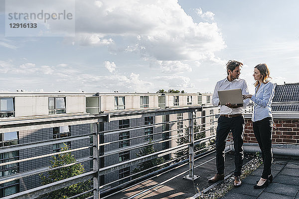 Business people standing on balcony,  discussing,  using laptop
