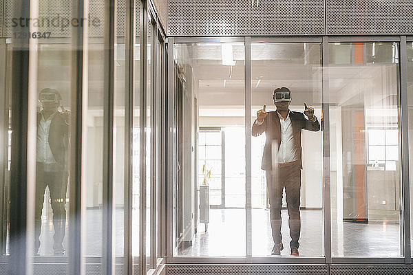 Businessman standing in office building,  looking through VR goggles