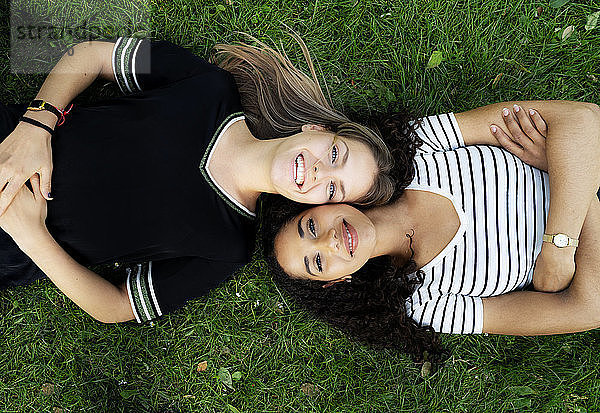 Two girlfriends relaxing in a park,  lying on grass
