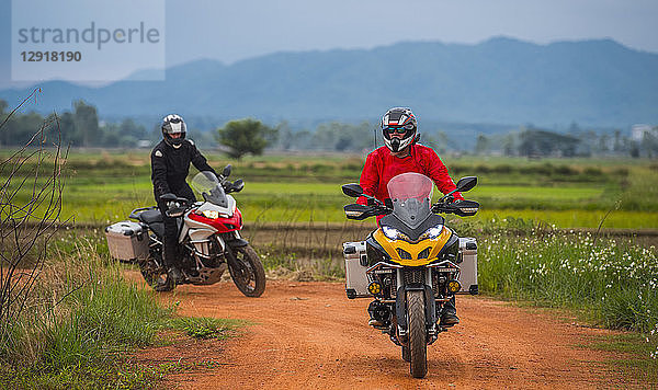 Zwei Männer auf Motorrädern auf einer leeren Schotterstraße mit einem Hügel im Hintergrund,  ¬ÝChiang¬ÝMai,  ¬ÝMueang¬ÝChiang Mai District,  Thailand
