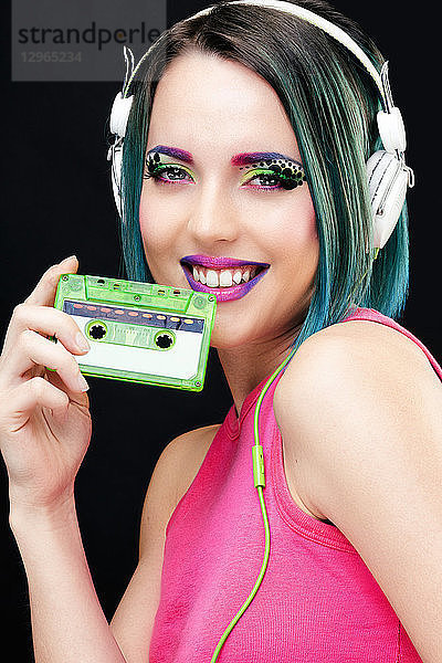 Porträt einer lächelnden jungen Frau,  die eine Audiokassette in der Hand hält