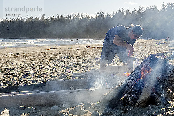 Mann,  der am Strand über einem Lagerfeuer Essen zubereitet, â€ Tofino,  British Columbia,  Kanada