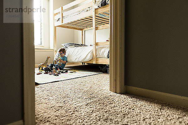 Junge spielt mit Spielzeug im Schlafzimmer mit Blick durch die Tür