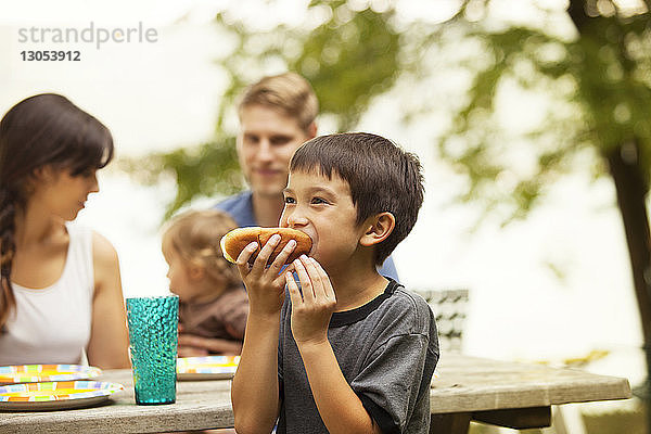 Junge isst Brot gegen Familie,  die am Picknicktisch sitzt