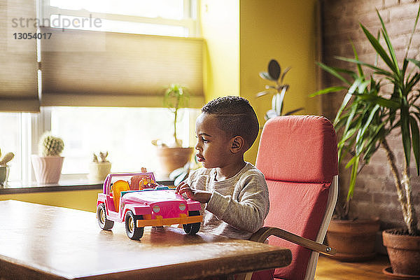 Junge spielt mit Spielzeugauto,  während er zu Hause auf einem Stuhl am Tisch sitzt