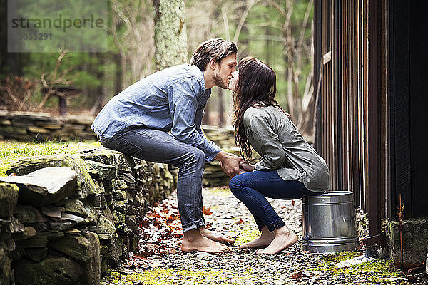 Seitenansicht eines Paares,  das sich auf den Mund küsst,  während es an einer Hütte sitzt