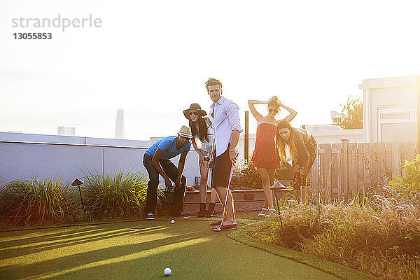Freunde schauen auf den Golfball,  während sie bei Sonnenuntergang auf der Terrasse des Gebäudes stehen
