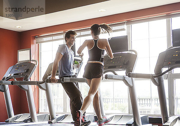 Glücklicher Mann schaut Frau an,  die im Fitnessstudio auf dem Laufband läuft