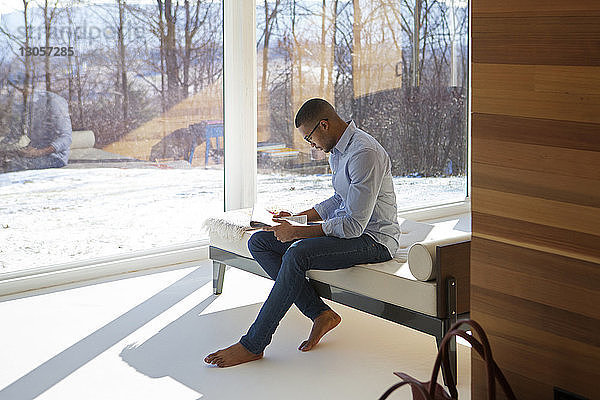 Seitenansicht eines Mannes,  der Zeitung liest,  während er zu Hause auf dem Sofa sitzt
