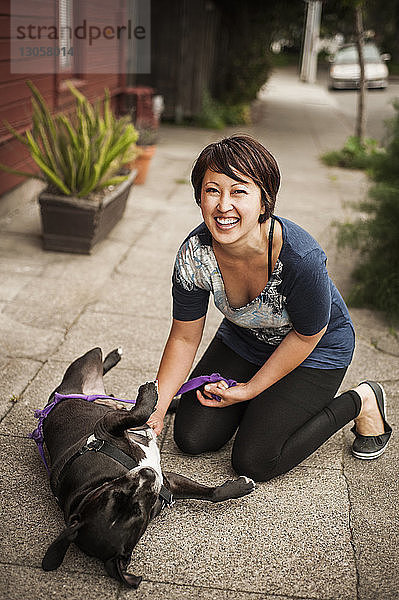 Porträt einer Frau,  die mit einem Hund auf einem Fußweg spielt