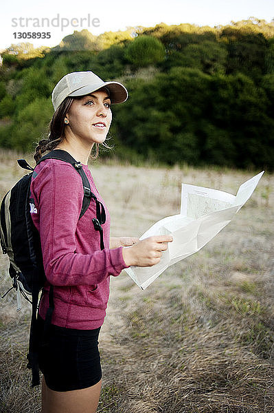 Seitenansicht einer Wanderin,  die die Karte hält,  während sie auf dem Feld steht