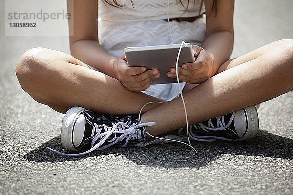 Unterer Teil eines Mädchens hält Tablette,  während es auf der Straße sitzt