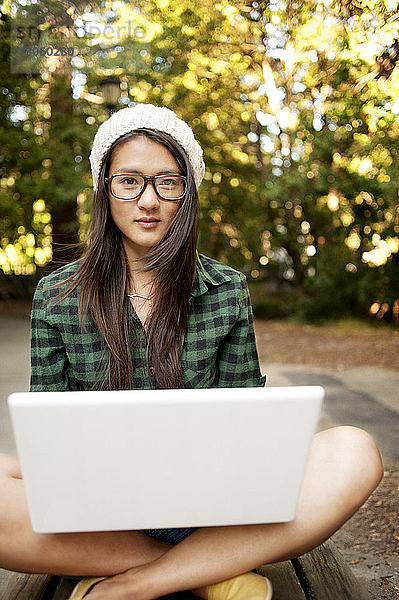 Porträt einer Frau,  die mit Laptop-Computer auf dem Feld sitzt