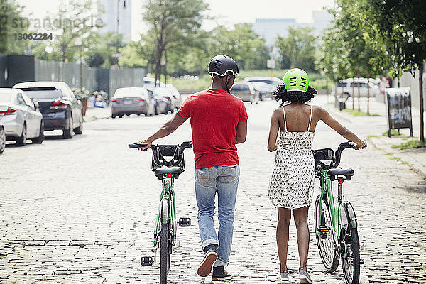Rückansicht eines Paares mit Fahrrädern,  das in der Stadt auf der Straße geht