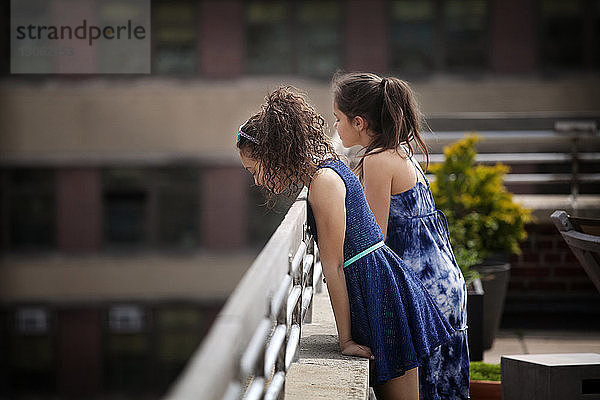 Seitenansicht von Mädchen,  die auf einem Geländer lehnen,  während sie auf der Gebäudeterrasse stehen