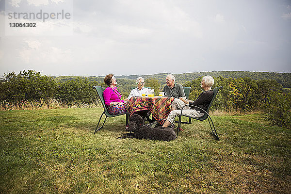 Ältere Freunde sitzen am Frühstückstisch im Rasen gegen den Himmel