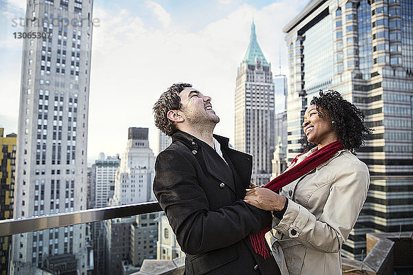Fröhliches Paar steht auf einer Terrasse mit Stadtgebäuden im Hintergrund