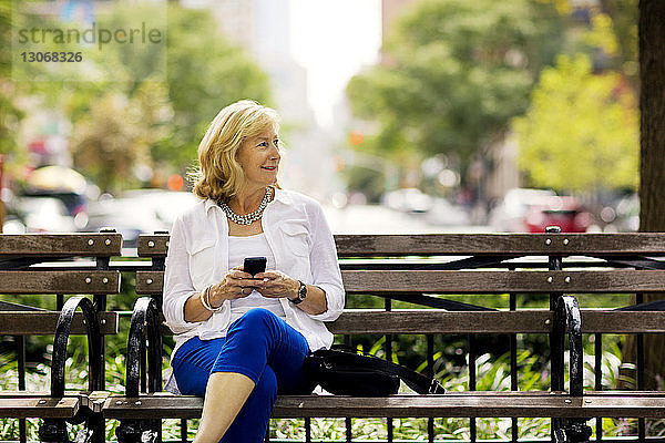 Frau schaut weg,  während sie in der Stadt ein Mobiltelefon benutzt